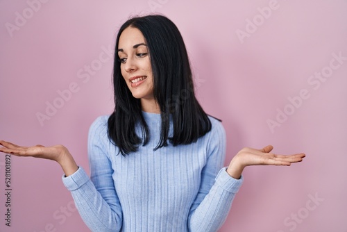 Hispanic woman standing over pink background smiling showing both hands open palms, presenting and advertising comparison and balance © Krakenimages.com