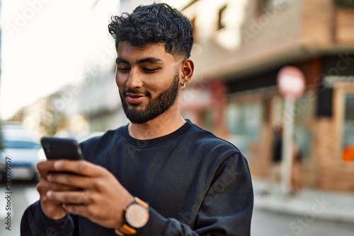 Young arab man smiling confident using smartphone at street