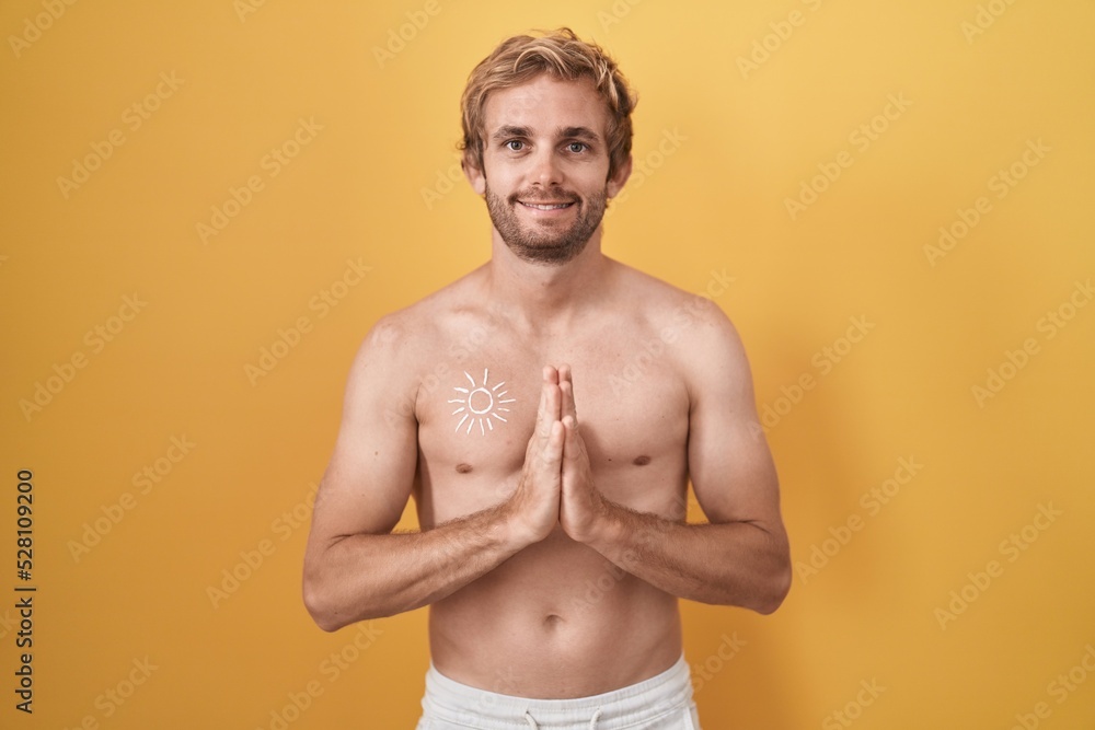 Fototapeta premium Caucasian man standing shirtless wearing sun screen praying with hands together asking for forgiveness smiling confident.
