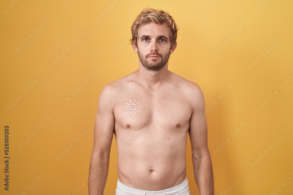 Caucasian man standing shirtless wearing sun screen relaxed with serious expression on face. simple and natural looking at the camera.
