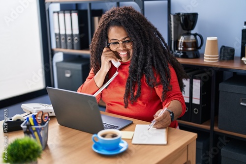 African american woman business worker talking on telephone writing on notebook at office