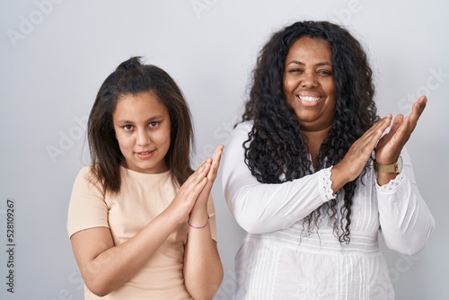 Mother and young daughter standing over white background clapping and applauding happy and joyful  smiling proud hands together