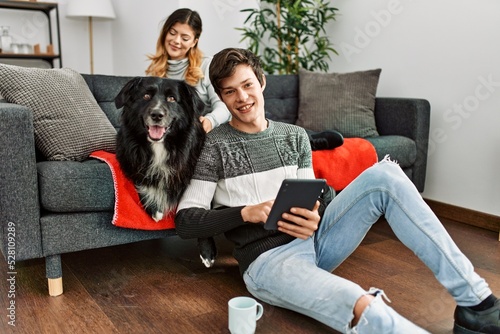 Young caucasian couple smiling happy with dog using touchpad at home.