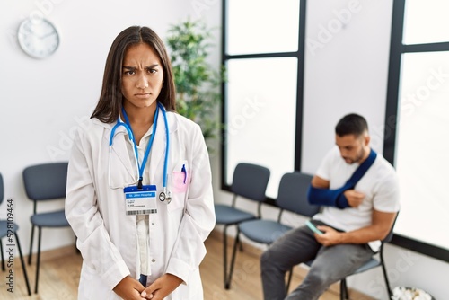 Young asian doctor woman at waiting room with a man with a broken arm skeptic and nervous  frowning upset because of problem. negative person.