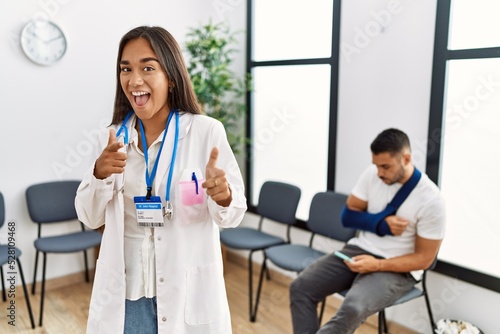 Young asian doctor woman at waiting room with a man with a broken arm pointing fingers to camera with happy and funny face. good energy and vibes.