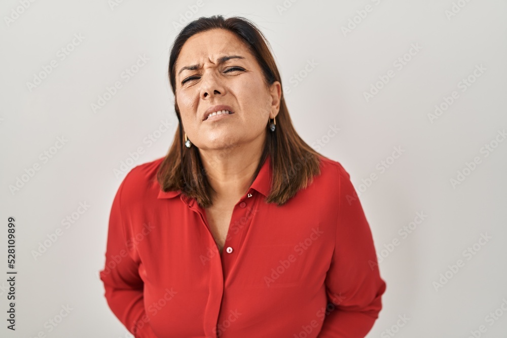 Hispanic mature woman standing over white background with hand on stomach because indigestion, painful illness feeling unwell. ache concept. Hispanic mature woman standing over white background with hand on stomach because indigestion, painful illness feeling unwell. ache concept.