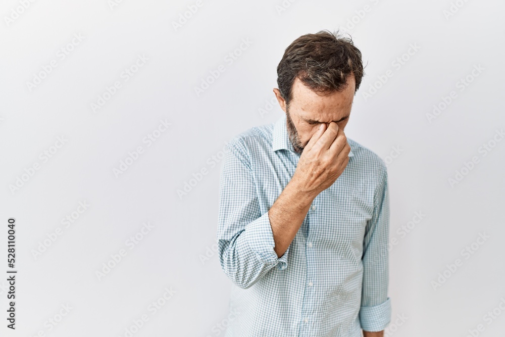 Middle age hispanic man with beard standing over isolated background tired rubbing nose and eyes feeling fatigue and headache. stress and frustration concept. Middle age hispanic man with beard standing over isolated background tired rubbing nose and eyes feeling fatigue and headache. stress and frustration concept.