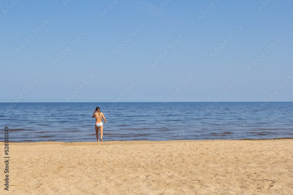 a girl enters the water on a lake with a sandy beach and no one is around