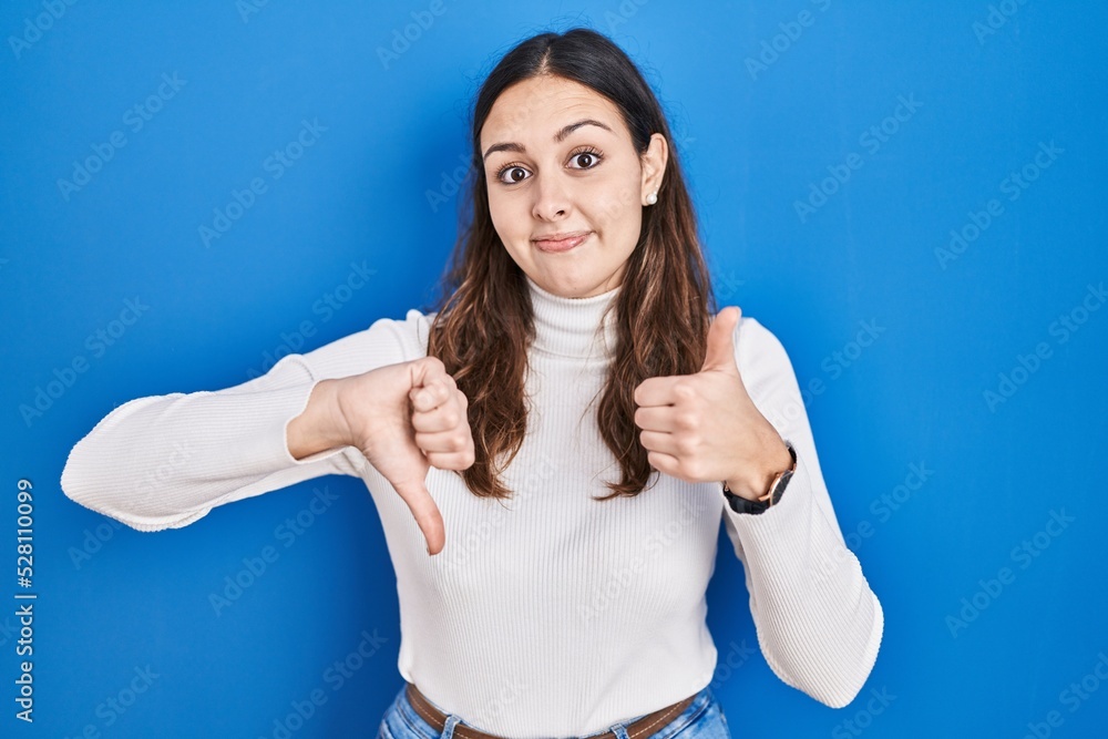 Fototapeta premium Young hispanic woman standing over blue background doing thumbs up and down, disagreement and agreement expression. crazy conflict