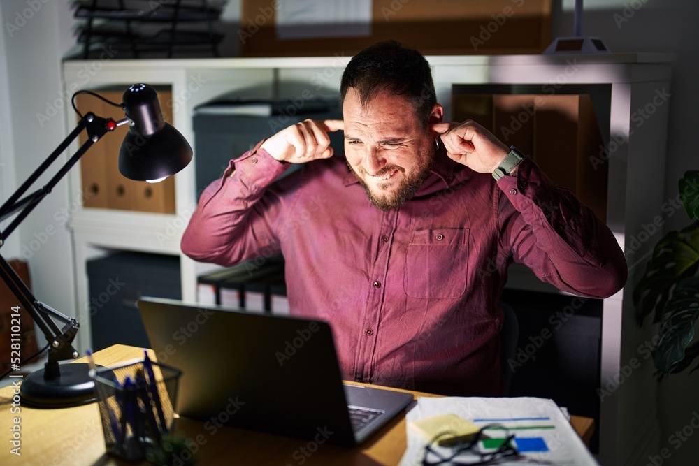 Plus size hispanic man with beard working at the office at night covering ears with fingers with annoyed expression for the noise of loud music. deaf concept. Plus size hispanic man with beard working at the office at night covering ears with fingers with annoyed expression for the noise of loud music. deaf concept.