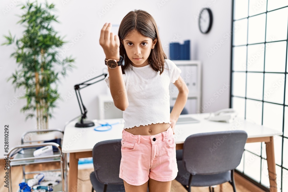 Young hispanic girl standing at pediatrician clinic doing italian gesture with hand and fingers confident expression Young hispanic girl standing at pediatrician clinic doing italian gesture with hand and fingers confident expression