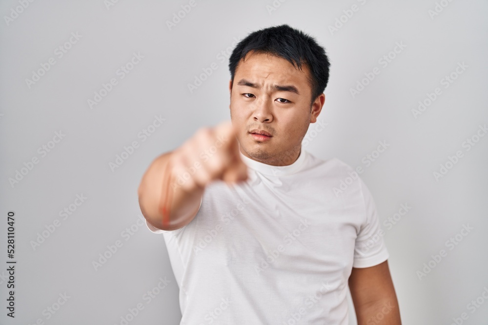 Young chinese man standing over white background pointing displeased and frustrated to the camera, angry and furious with you Young chinese man standing over white background pointing displeased and frustrated to the camera, angry and furious with you
