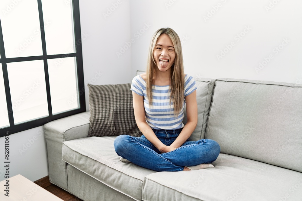 Asian young woman sitting on the sofa at home sticking tongue out happy with funny expression. emotion concept. Asian young woman sitting on the sofa at home sticking tongue out happy with funny expression. emotion concept.
