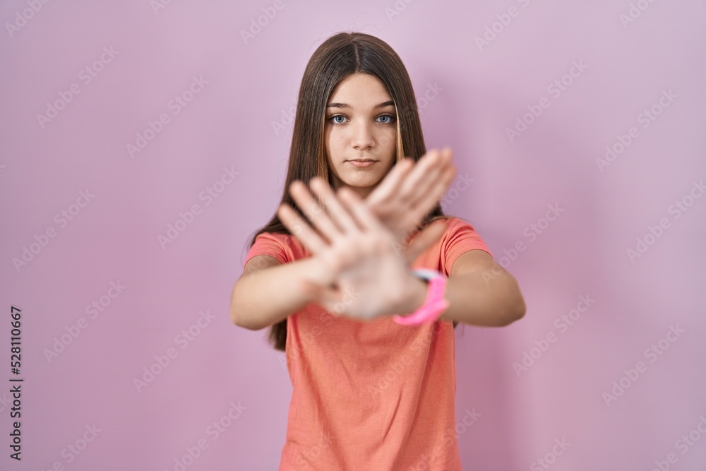 Teenager girl standing over pink background rejection expression crossing arms and palms doing negative sign, angry face Teenager girl standing over pink background rejection expression crossing arms and palms doing negative sign, angry face