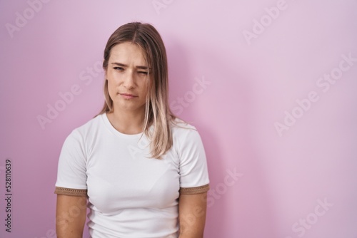 Blonde caucasian woman standing over pink background skeptic and nervous, frowning upset because of problem. negative person.