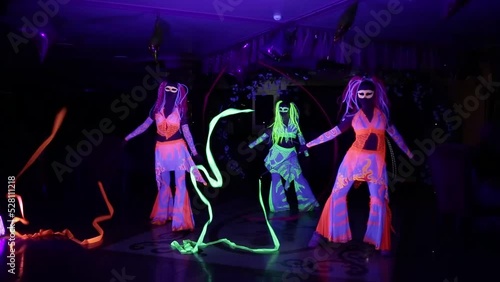 Dancers in glowing neon costumes perform in a dark room