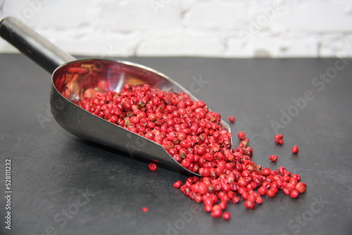 Pink pepper berries (Schinus terebinthifolia) in a stainless steel measuring spoon on a black surface, front view. photo