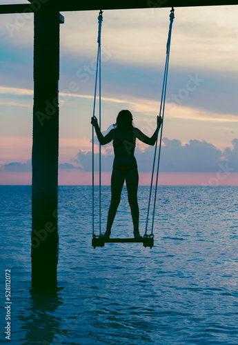 silhouette teen girl on a swing in the sea at sunset in the Maldives, the concept of travel and the beautiful nature