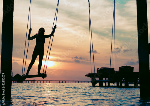 silhouette teen girl on a swing in the sea at sunset in the Maldives, the concept of travel and the beautiful nature