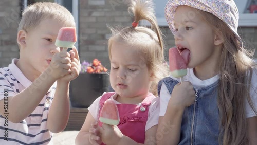 Three cute little Children enjoys delicious ice cream cone. Child eating watermelon popsicle. Kids Siblings snack sweets in Home Garden. Summer holiday Hot weather Sunny Day. Childhood, Food Candy