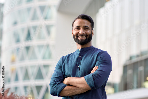Fotografia Happy confident wealthy young indian business man leader, successful eastern professional businessman crossing arms looking at camera posing outdoors in urban big city for close up headshot portrait