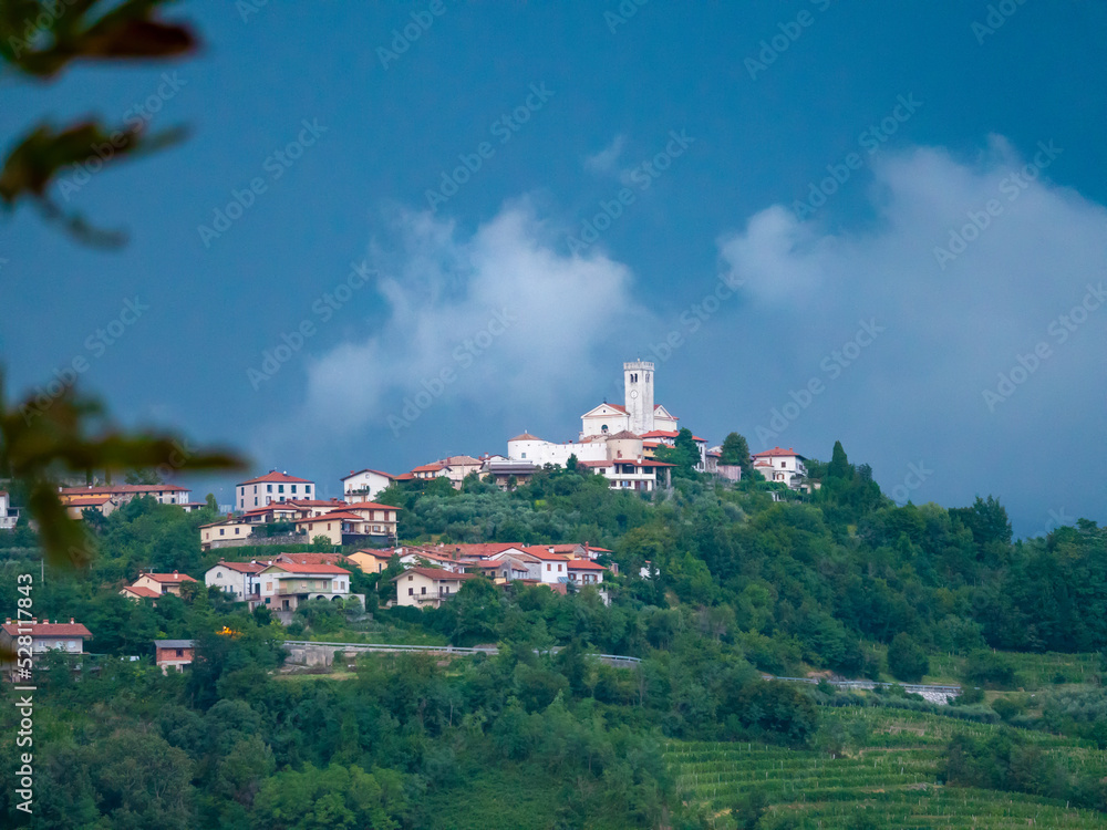 View of little town on hilltop surrounded with lush trees under dark blue sky