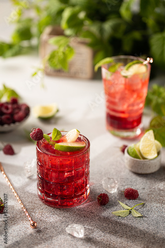 Women's hand pours liquer in raspberry cocktail with fresh berries and limes on the table with juicy greenery.healthy,detox drinks.
