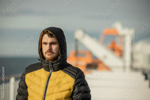 Person on a ferry in yellow and black jacket. Young fisherman male standing on a deck of a ship. photo