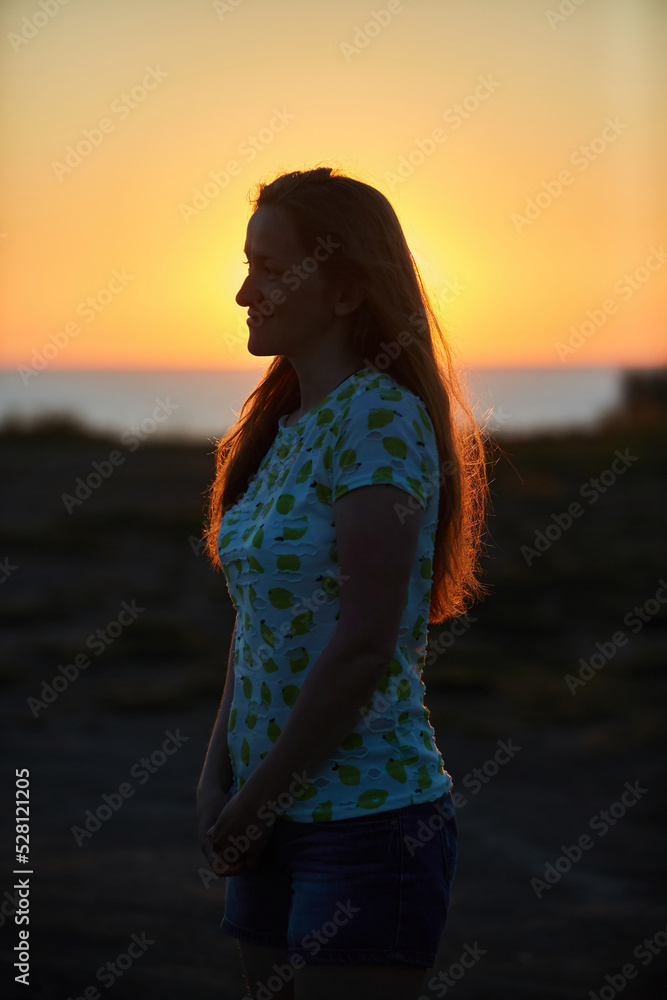 Portrait of a beautiful young girl at sunset against the background of nature and the sea. Portrait of a beautiful young girl at sunset against the background of nature and the sea.