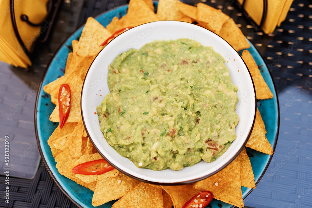 Top view of woman hand holding tortilla chips or nachos with tasty guacamole dip Top view of woman hand holding tortilla chips or nachos with tasty guacamole dip