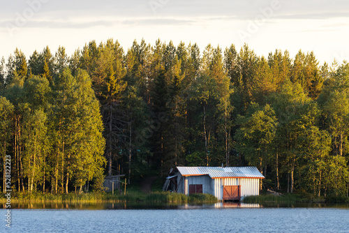 Fotografiet A small boathouse on the bank of a lake in summery Finland