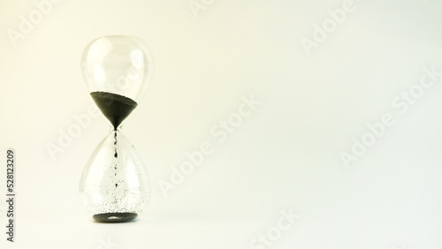 Hourglass on a white background. Black sand flows down the transparent glass. copy space.