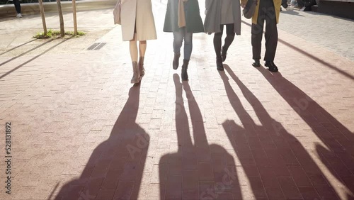 Feet of four unrecognizable faceless people walk outside on a sunny day in a corporate business district. photo