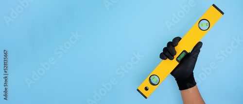 Hand wearing black gloves holding yellow black water level isolated baby blue background with copy space