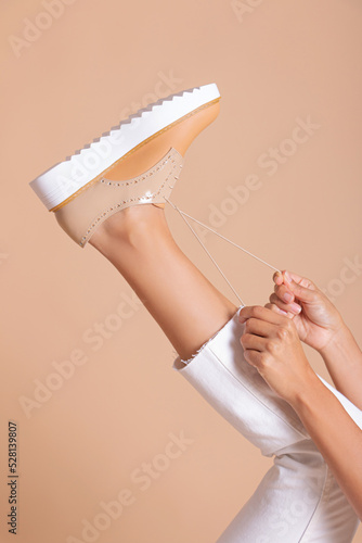 Legs of a woman close-up, sneakers with design in studio on cream background. © Wilson