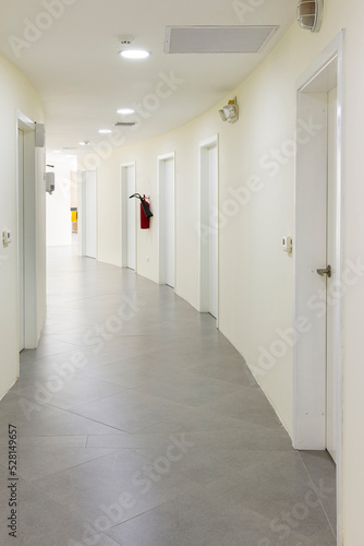 Hallway of a building with several doors and access to different rooms  all in white and ceramic floor. Vertical photography.