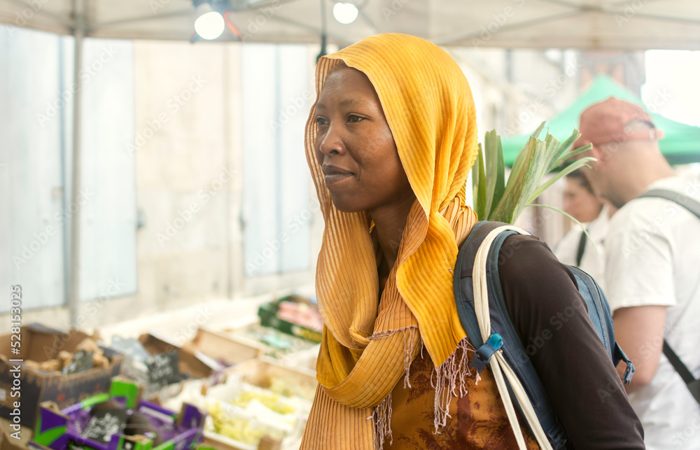 Young black Muslim woman in hijab on a market food, outdoors, African Islamic lady buying vegetables in the street with backpack, open space.