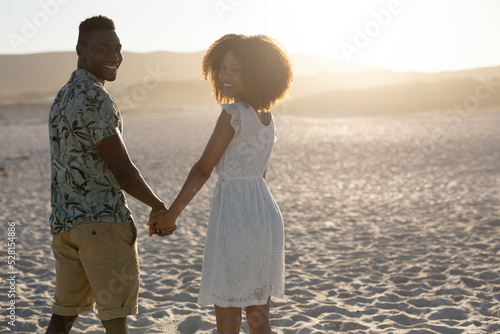 Mixed race couple holding hands and smiling into the camera on a sunny day