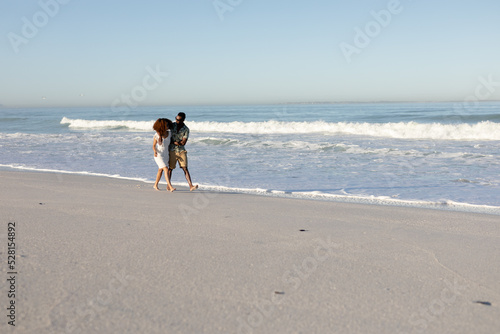 A mixed race couple walking and laughing on beach on a sunny day