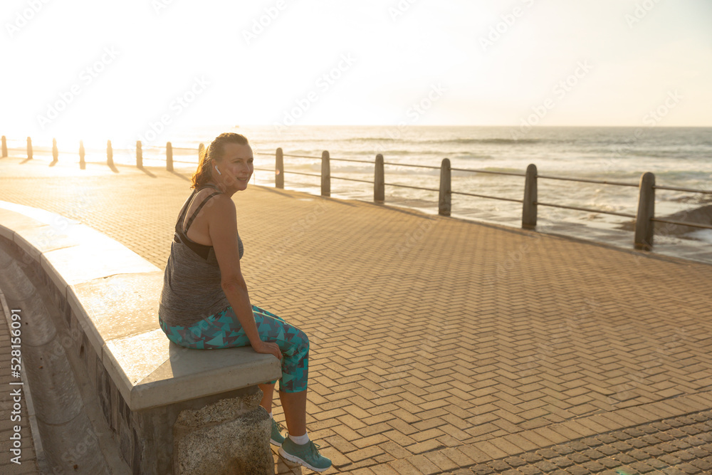 Female jogger sitting on bench on seaside