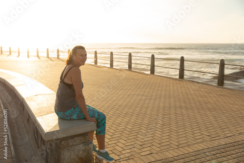 Female jogger sitting on bench on seaside