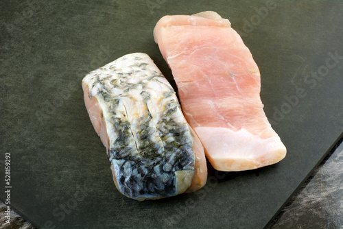 Two raw barramundi fish fillet slices on black cutting board