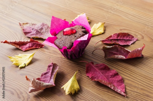 Fototapeta Naklejka Na Ścianę i Meble -  Homemade chocolate cupcake on a wooden background and autumn leaves. Sweet autumn baking concept.