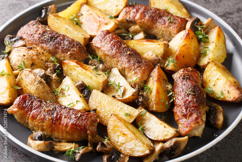 Baked beef rolls with potato wedges, mushrooms and thyme on plate closeup on the table. Horizontal photo