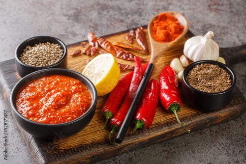 Traditional homemade harissa hot chili pepper sauce paste with garlic and olive oil on the bowl on wooden board with ingredients closeup. Horizontal photo