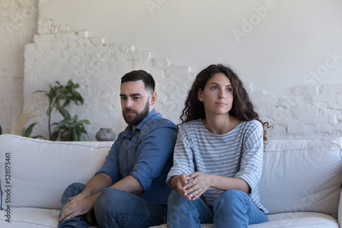 Silent couple sit on sofa staring aside after fight, avoid talk, look deep in thoughts about relationship break up, troubles in relations. Marriage, split, crisis, misunderstanding, quarrels concept photo