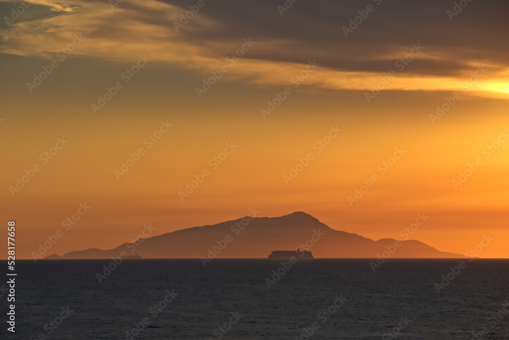 Cruise passengers ship silhouette passing before Ischia mountain in the far-off, in the Gulf of Naples, at golden hour.