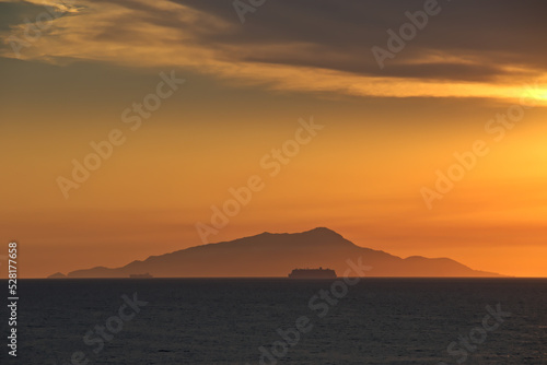 Cruise passengers ship silhouette passing before Ischia mountain in the far-off, in the Gulf of Naples, at golden hour.