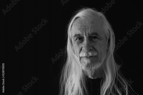 Low key studio black and white portrait of smiling attractive old man with loose long gray hair. Horizontally. 