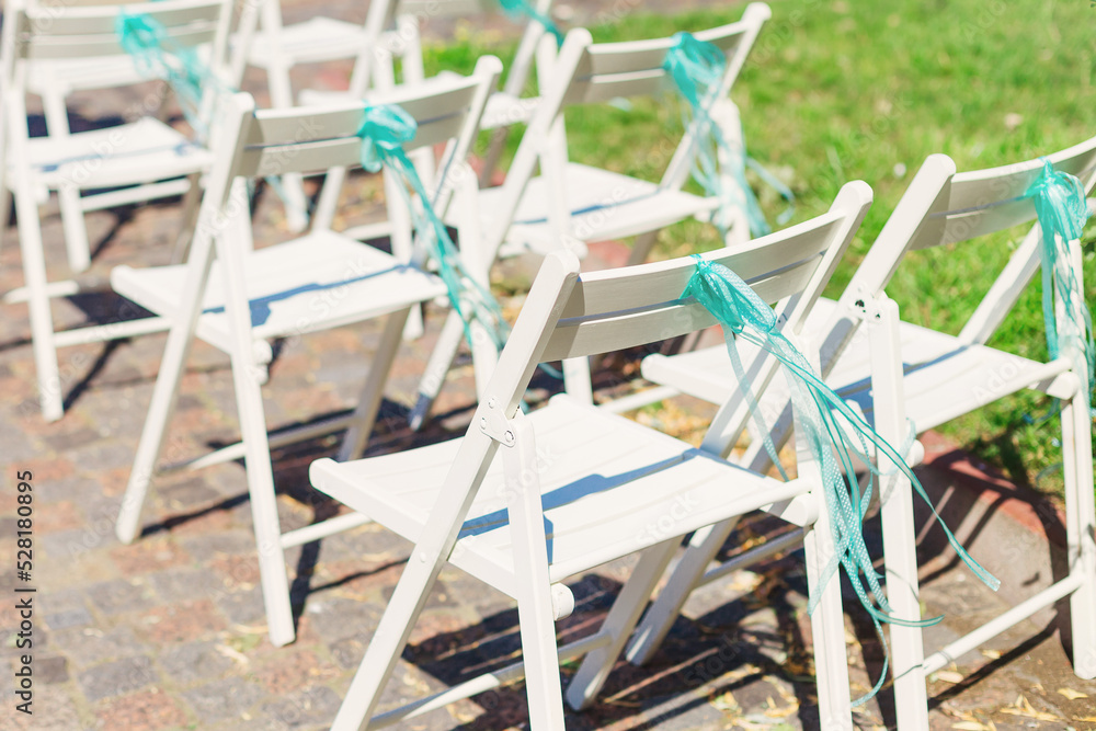 Close-up of white armchairs with turquoise bow. sunny day